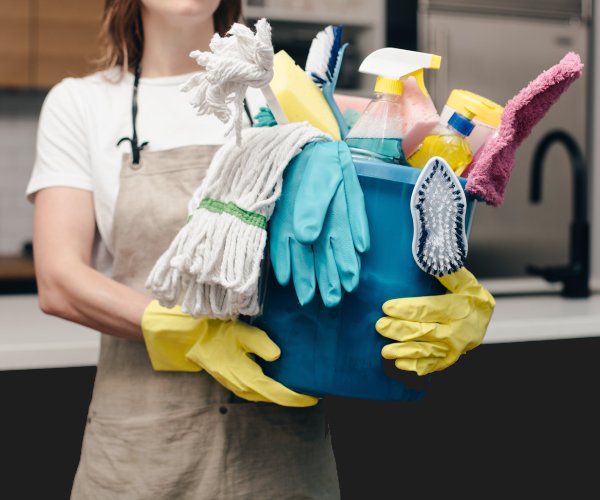 Professional house cleaner holding a bucket of cleaning supplies in a kitchen